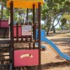 Parco giochi con scivolo blu e alberi intorno.