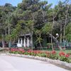 Un piccolo edificio bianco circondato da alberi e fiori rossi lungo un vialetto.