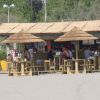 Chiosco in spiaggia con tetto di paglia e tavolini all'aperto.